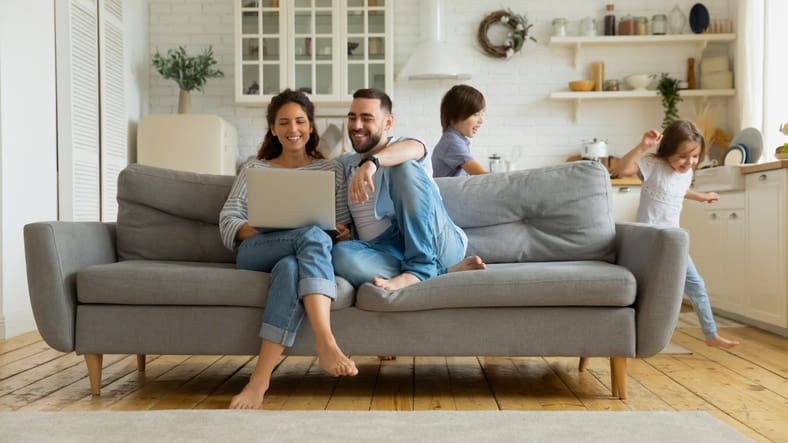 family-on-computer Couple on couch looking at laptop while two children play nearby
